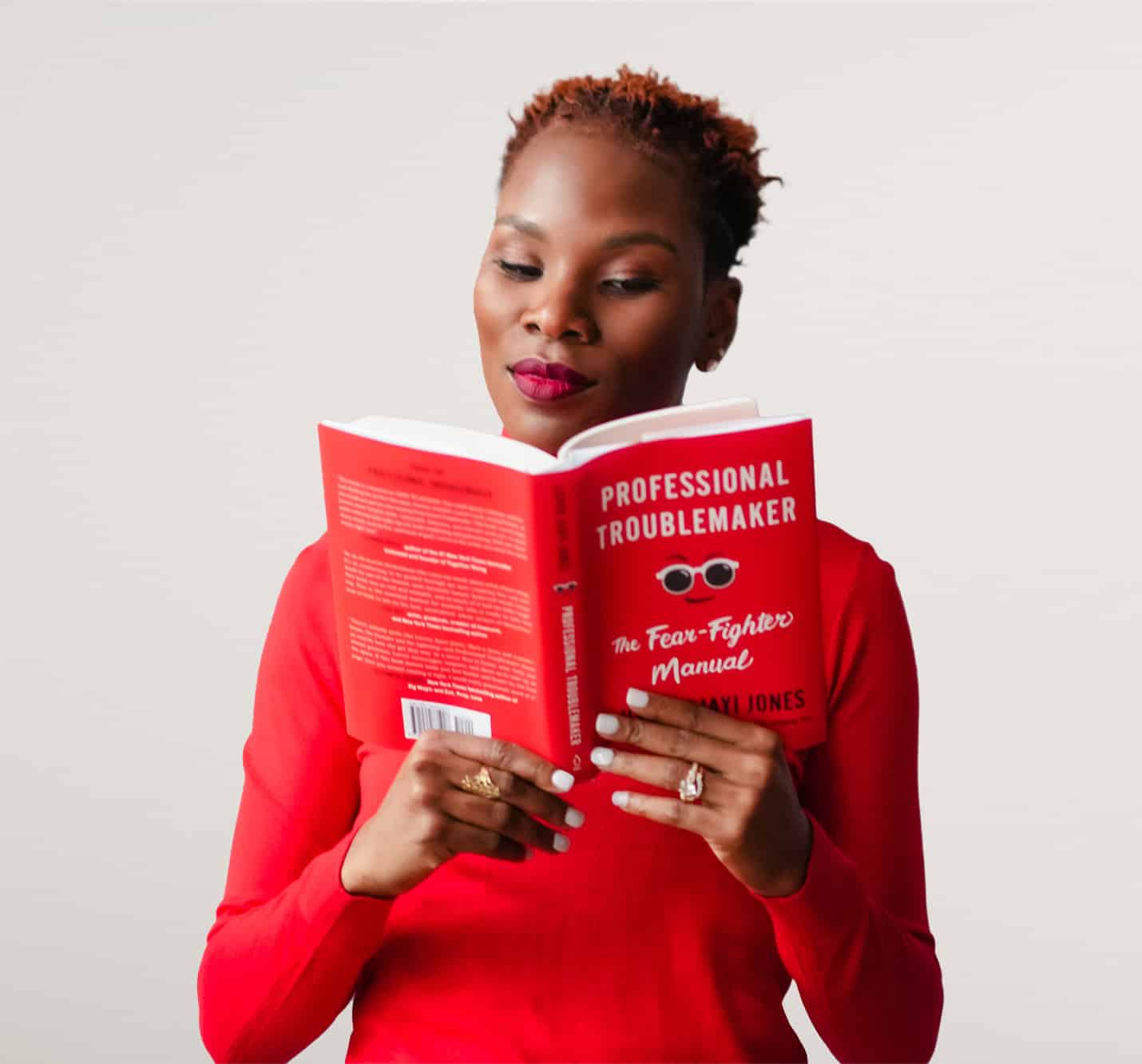 Luvvie in red shirt reading her book Professional Troublemaker