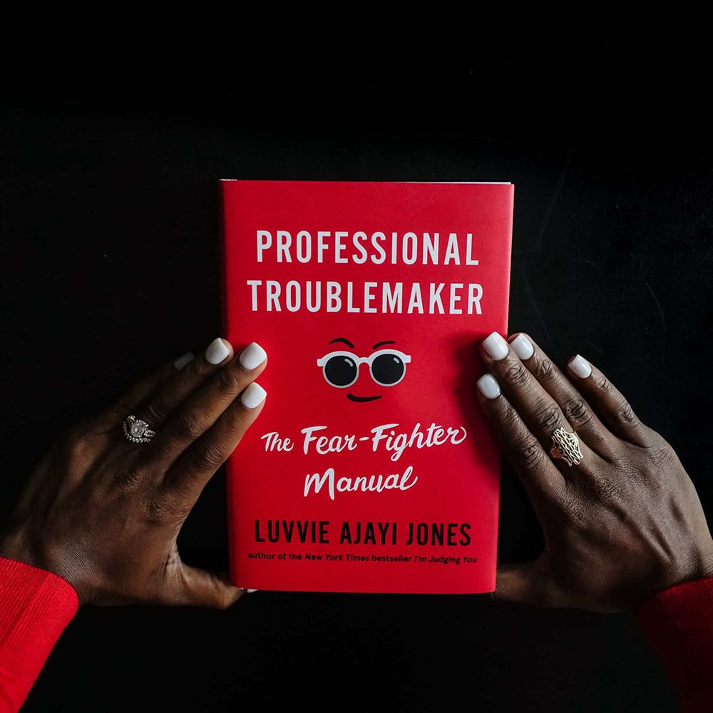 Aerial shot of Professional Troublemaker book with Luvvie's hands on top of the cover