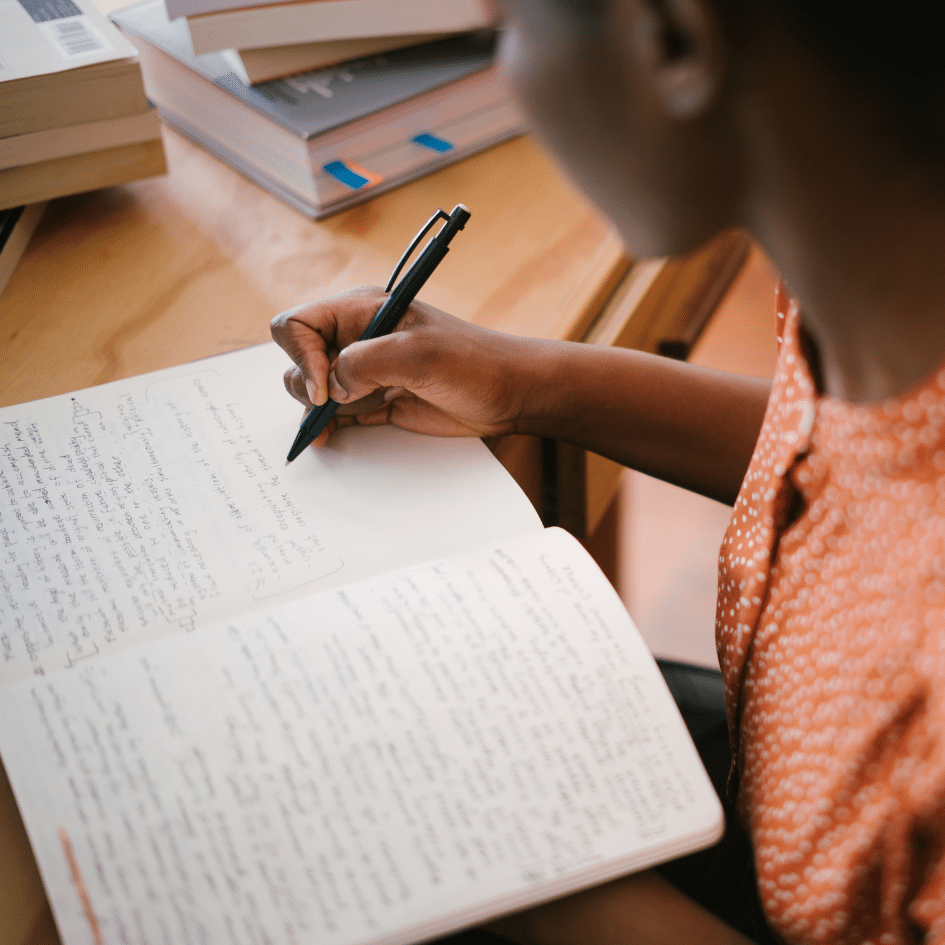 close up view of woman in orange shirt writing in notebook at a desk