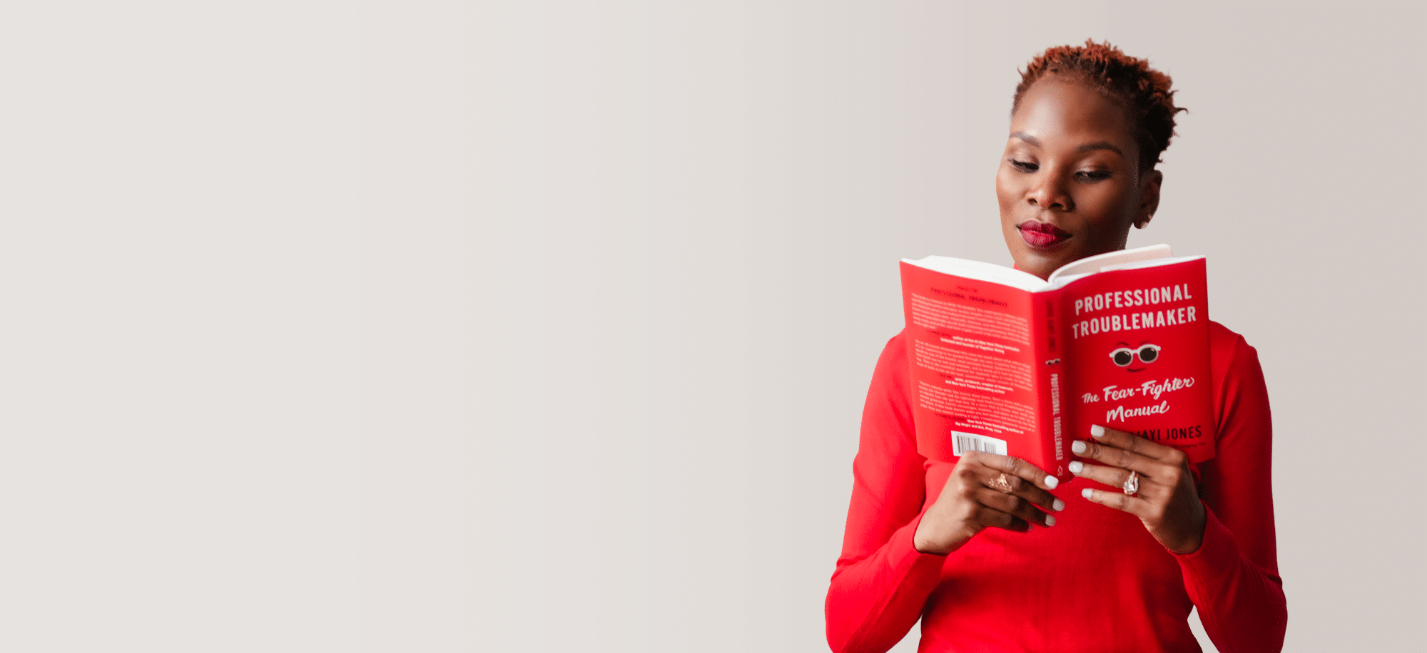 Luvvie in red shirt reading her book Professional Troublemaker